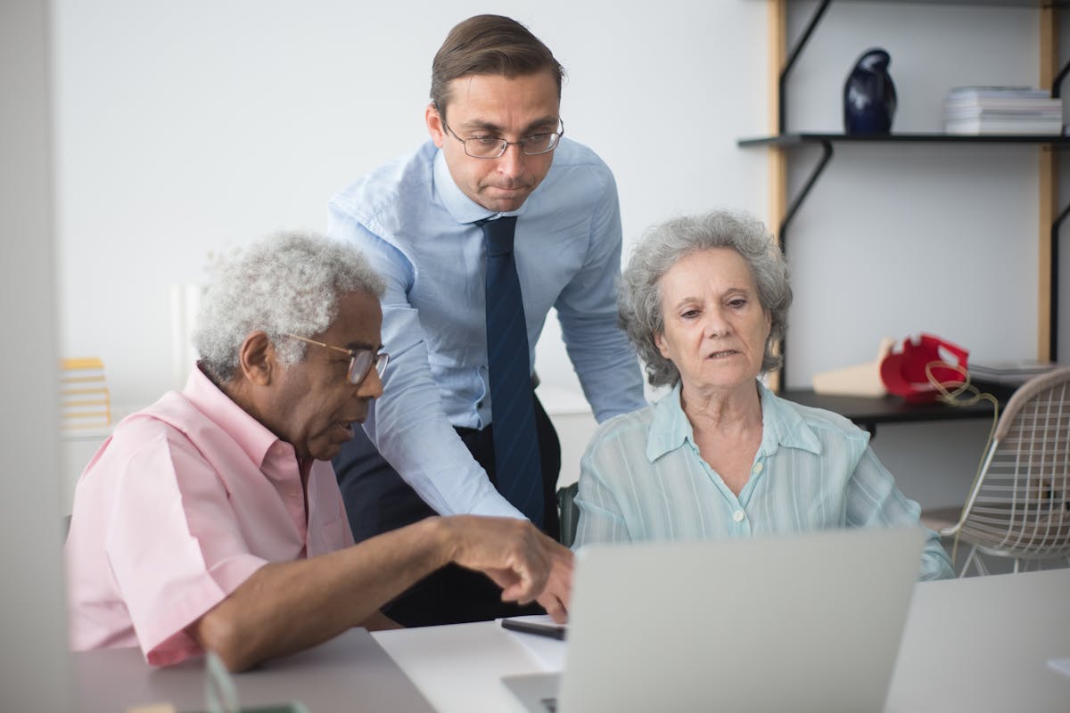 A Man Standing Between Elderly People Sitting at a Desk